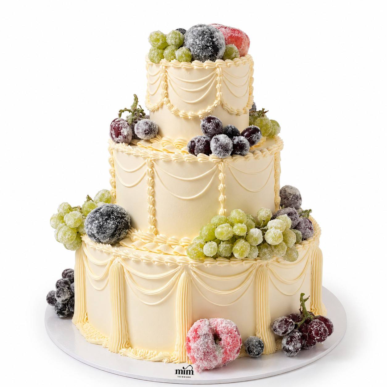 Frosted Grape Vintage Cake Three-tier ivory vintage cake with elegant piping, decorated with frosted green and dark grapes for a luxurious finish. عيد ميلاد أطفال برايد ملجه 1200 Frosted Grape Vintage Cake - Image 1